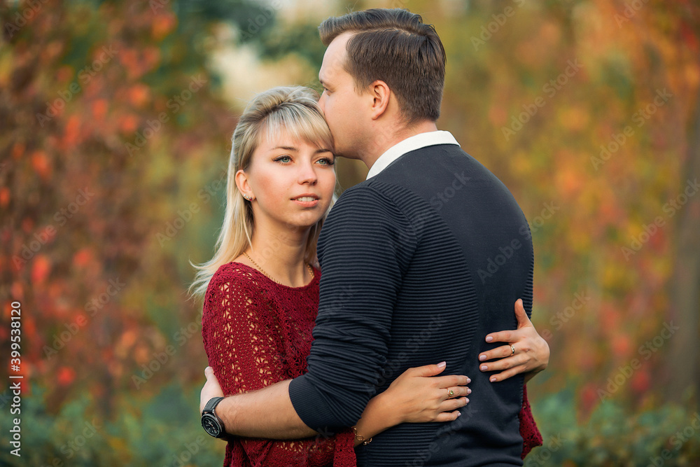 blonde girl in maroon sweater, brown-haired young man in blue sweater hug in the Park blonde girl in maroon sweater, brown-haired young man in blue sweater hug in the Park