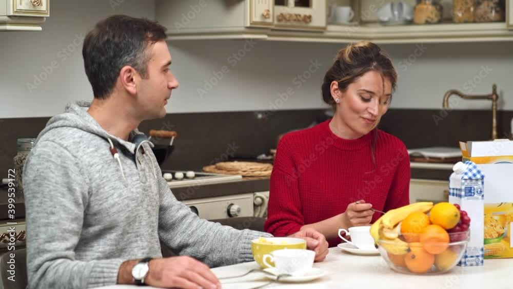 CHISINAU, MOLDOVA - SEPTEMBER 25, 2018: A couple talking on a kitchen. Looking at each other and smiling. Woman holding a cup of tea. Table with food CHISINAU, MOLDOVA - SEPTEMBER 25, 2018: A couple talking on a kitchen. Looking at each other and smiling. Woman holding a cup of tea. Table with food