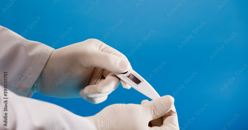 digital thermometer in doctor's hand with surgical glove and blue background.