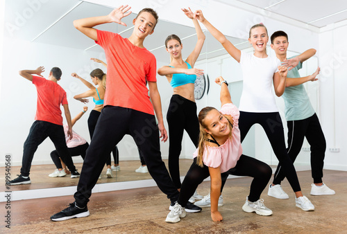 Cheerful smiling teenage boys and girls having fun in choreography class, posing with female trainer
