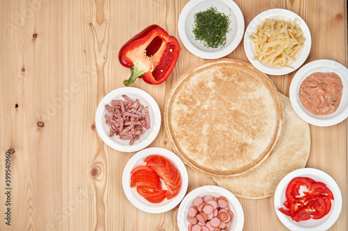 Composition of fresh pizza ingredients on a light wooden background. Cooking pizza. Top view with copy space.