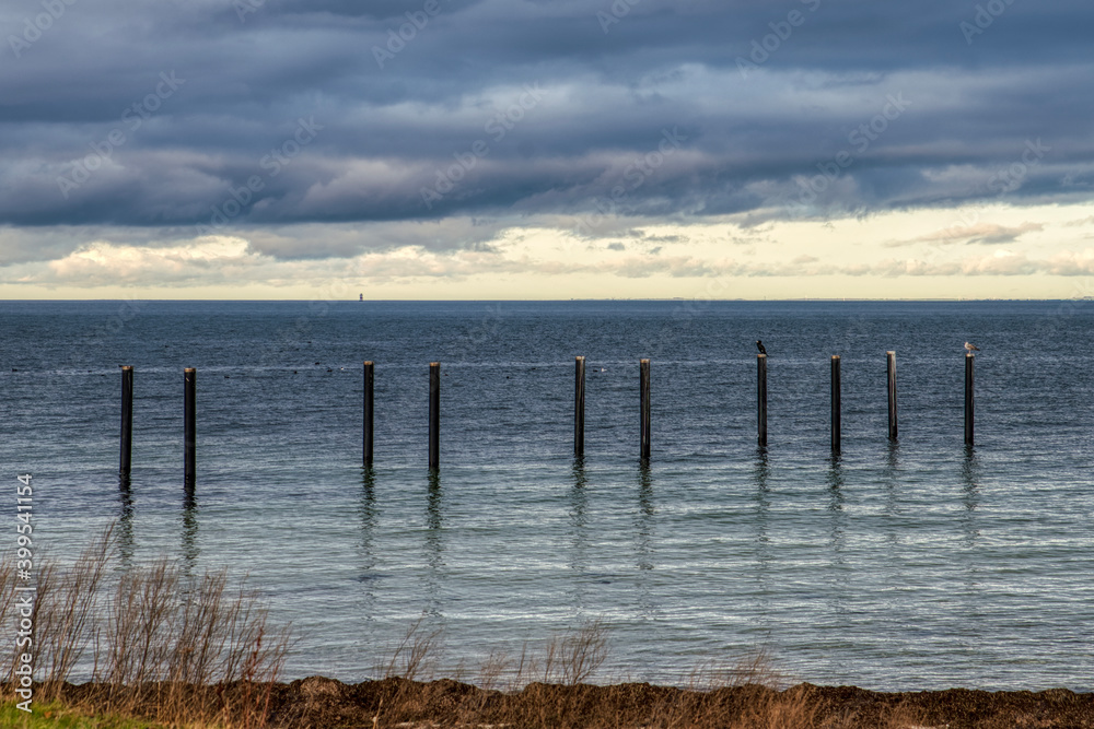 Isolated industrial mooring poles in the Baltic sea with birds on them in Limhamn. Old mooring masts in the Oresund strait with thick clouds convey sadness, uncertainty and melancholy - Malmo, Sweden