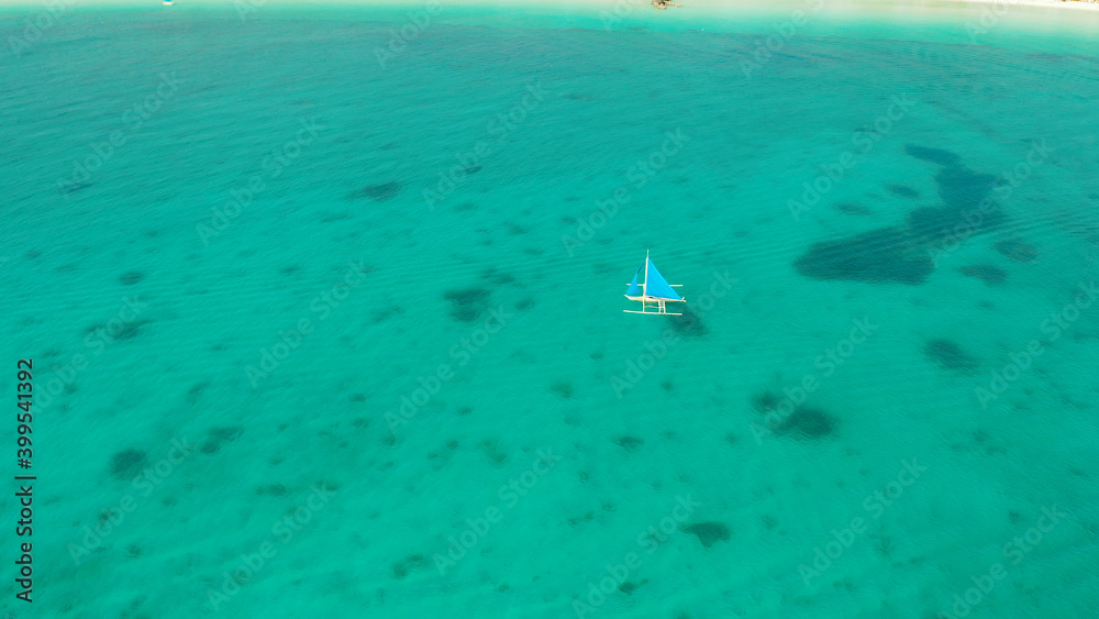 Sailing yacht in crystal clear turquoise water, aerial view. Sailing boat glides over the waves, Boracay, Philippines.