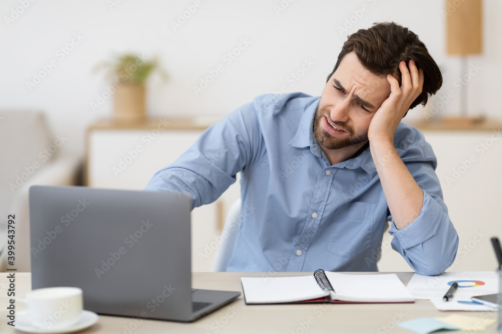 Unhappy Man Sitting At Laptop Looking At Screen At Workplace Unhappy Man Sitting At Laptop Looking At Screen At Workplace