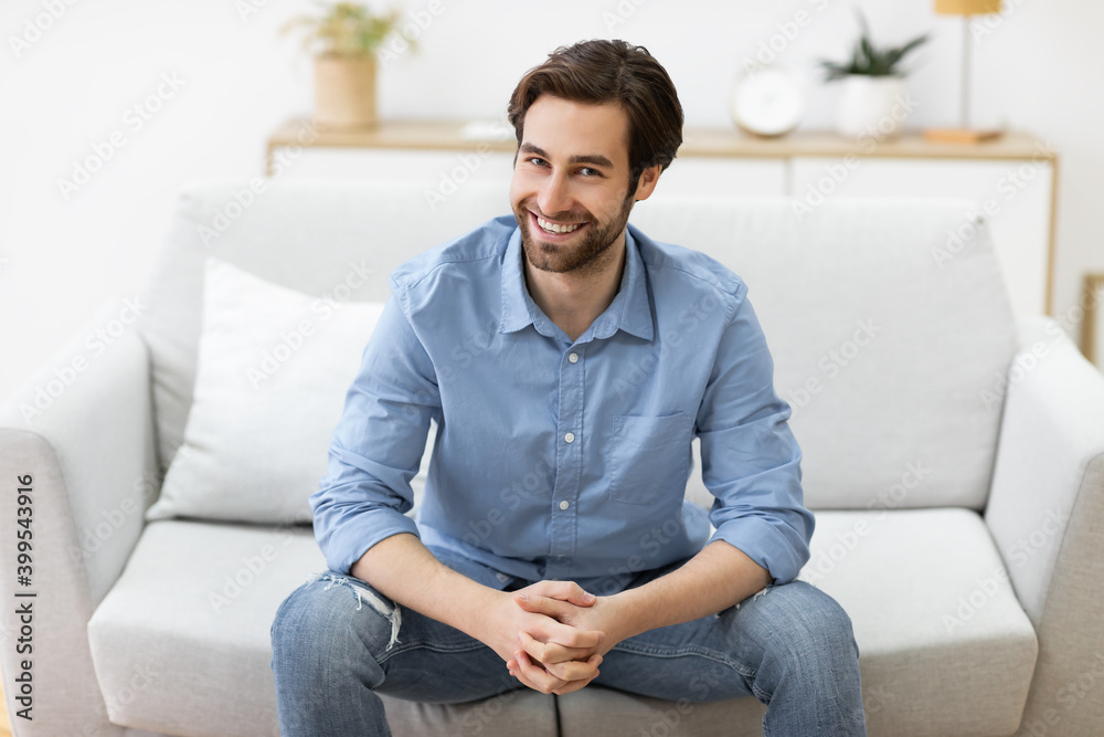 Guy Sitting On Sofa Smiling To Camera Posing At Home