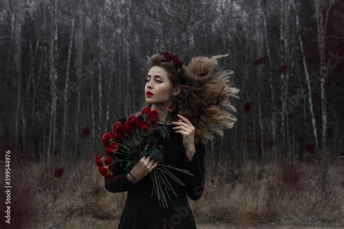 Russia, Moscow - 11/14/2020: A beautiful girl with curly blond hair stands in a black dress with flowers.