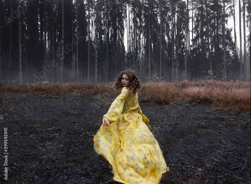 A girl in a gloomy misty forest in a bright yellow dress. the girl got lost in the thicket.