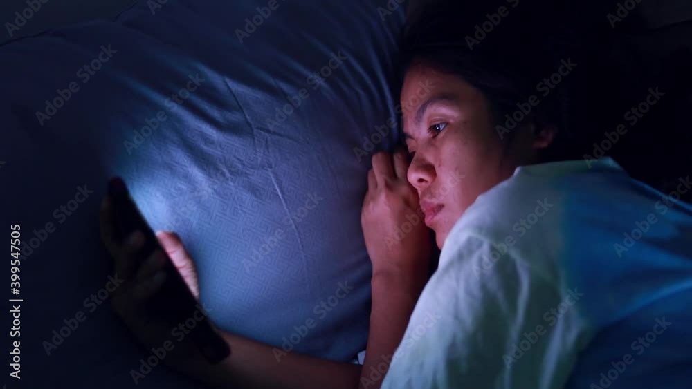 Asian woman sleeps late using a smartphone in the dark at the bed Asian woman sleeps late using a smartphone in the dark at the bed