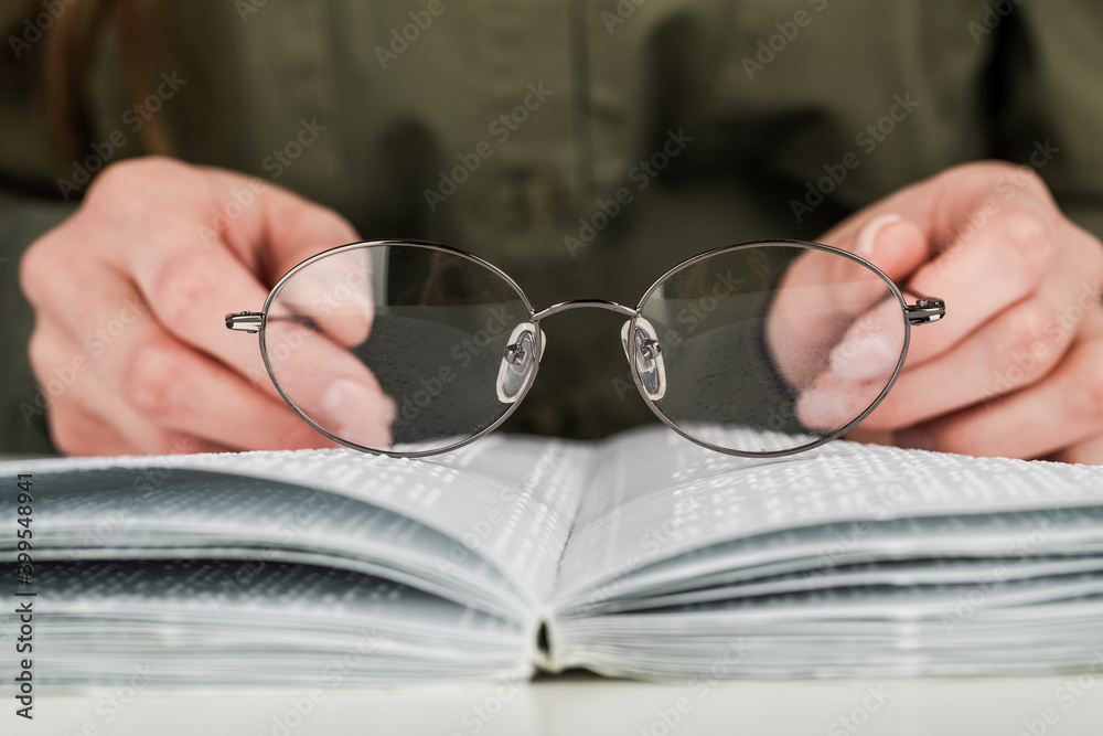 A woman holds black-rimmed glasses against the background of an open textbook reading books in Braille A woman holds black-rimmed glasses against the background of an open textbook reading books in Braille