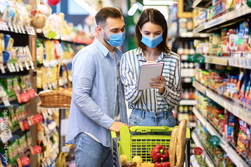 Couple Wearing Face Masks In Supermarket, Checking Shopping List