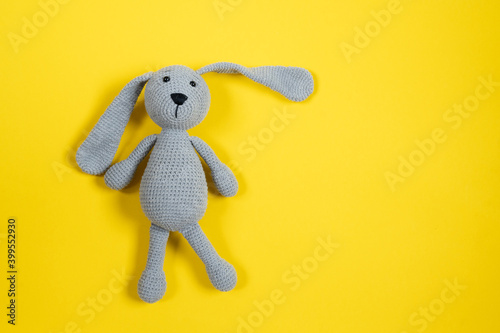 Grey knitted toy rabbit on yellow background with copy space. Top view