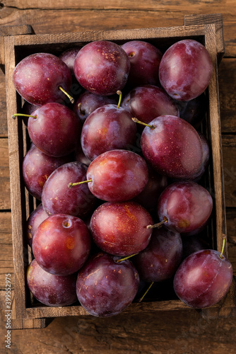 Fresh plums in crate on rustic wooden table. Top view. Close up