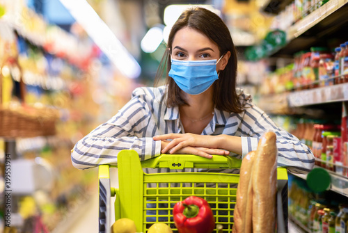 Young woman in mask with the cart shopping in supermarket