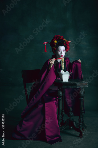 Delicious food. Young japanese woman as geisha isolated on dark green background. Retro style, comparison of eras concept. Beautiful female model like bright historical character, old-fashioned.