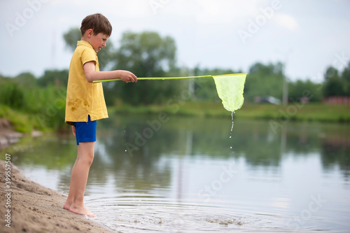 A little boy with a butterfly net is fishing in the lake. photo