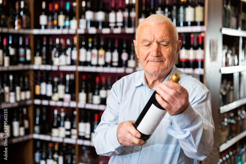 Elderly man chooses red wine in a liquor store. High quality photo
