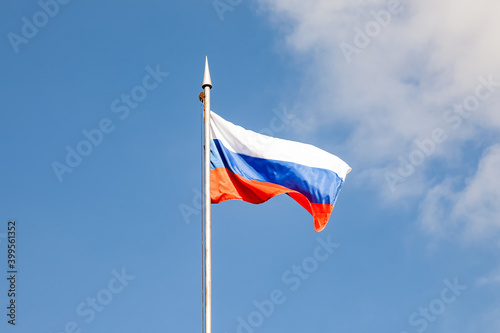 The flag of the Russian Federation flutters in the wind against the blue sky