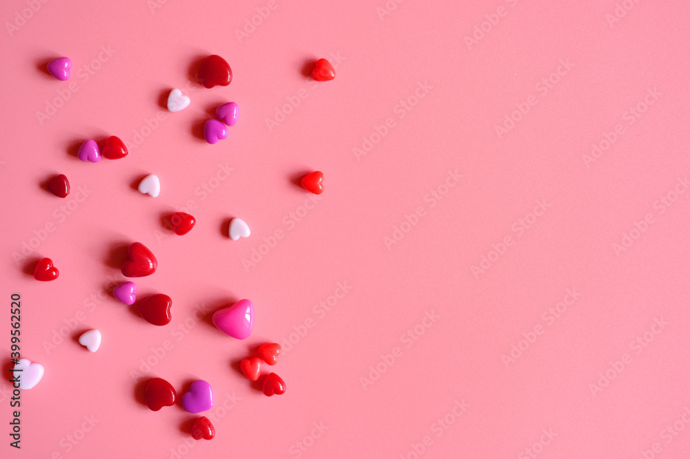 a heap of heart shaped glossy beads in different pink shades on a pink background. space for text