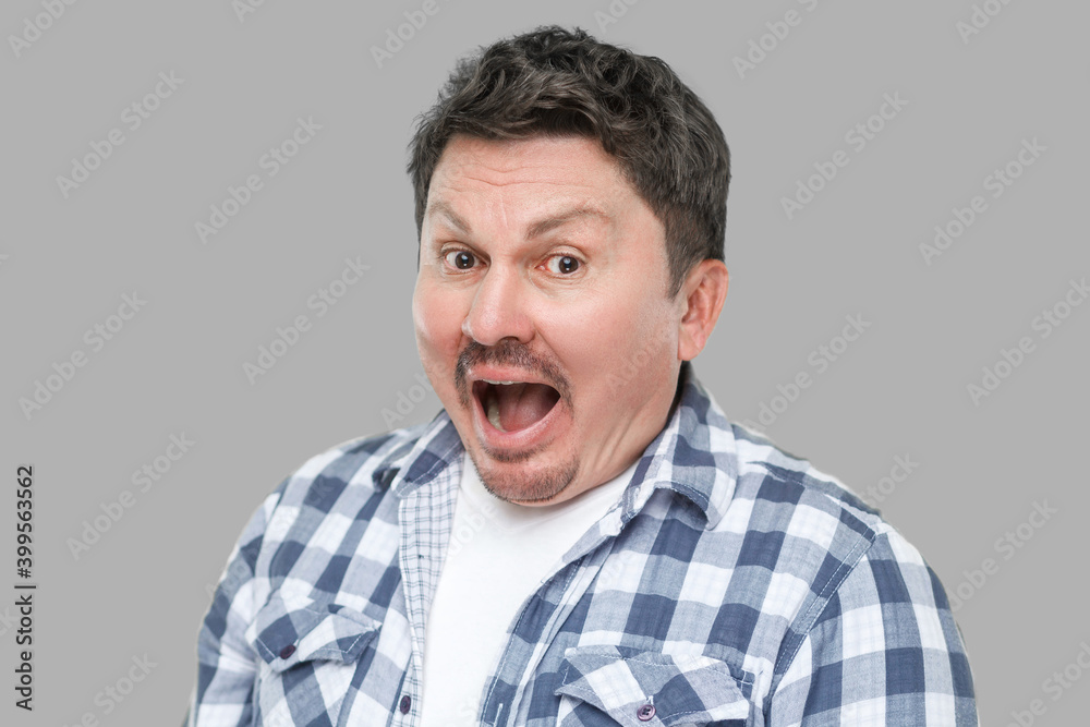 Fototapeta premium Closeup portrait of surprised handsome middle aged business man with mustache in casual checkered shirt standing with amazed face, looking at camera. indoor studio shot, isolated on gray background.