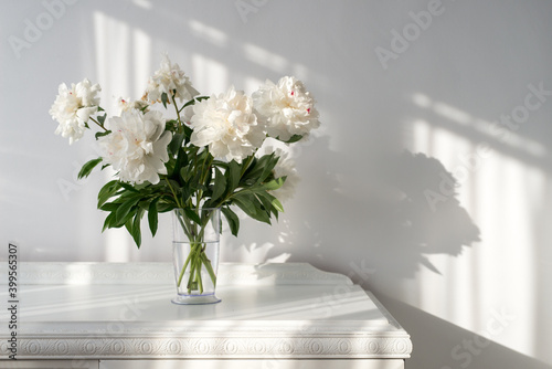Fototapeta Naklejka Na Ścianę i Meble -  white peonies in a vase on a white vintage table and beautiful shadows on the wall - copy space