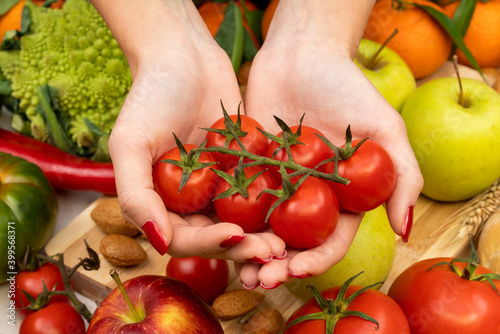 Hands of a girl with red nails holding cherry tomatoes on a table with various types of vegetables