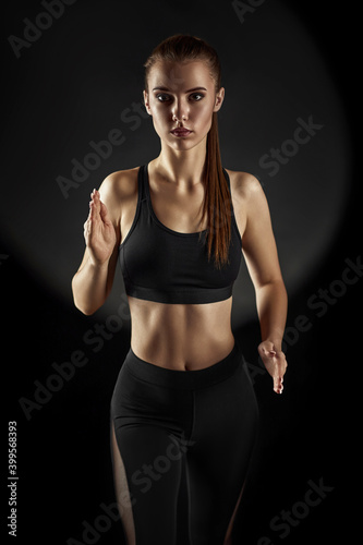 Strong sporty beautiful woman in black sportswear running on dark background. sport and fitness concept