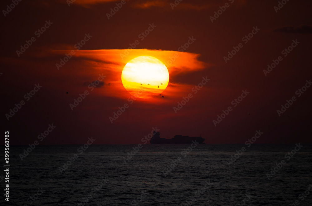 A beautiful Sun during sunset, with seagulls flying and cargo ship silhouette, Vila do Conde, Portugal.