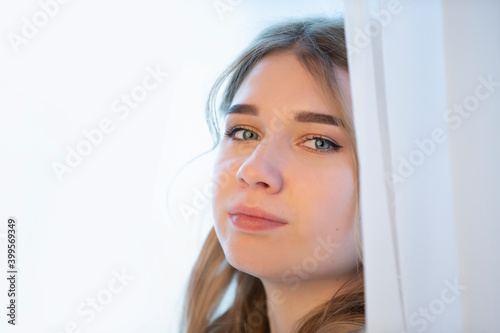 Close-up of the face of a young girl peeping out of the curtains.