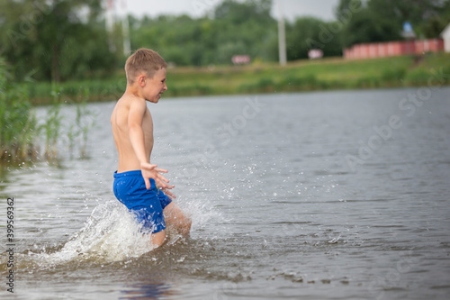Fototapeta Naklejka Na Ścianę i Meble -  A little boy runs into a cold river. The child swims in the lake in summer.