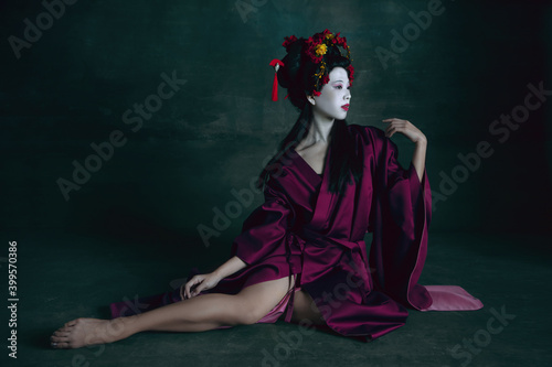 Beautiful. Young japanese woman as geisha isolated on dark green background. Retro style, comparison of eras concept. Beautiful female model like bright historical character, old-fashioned.