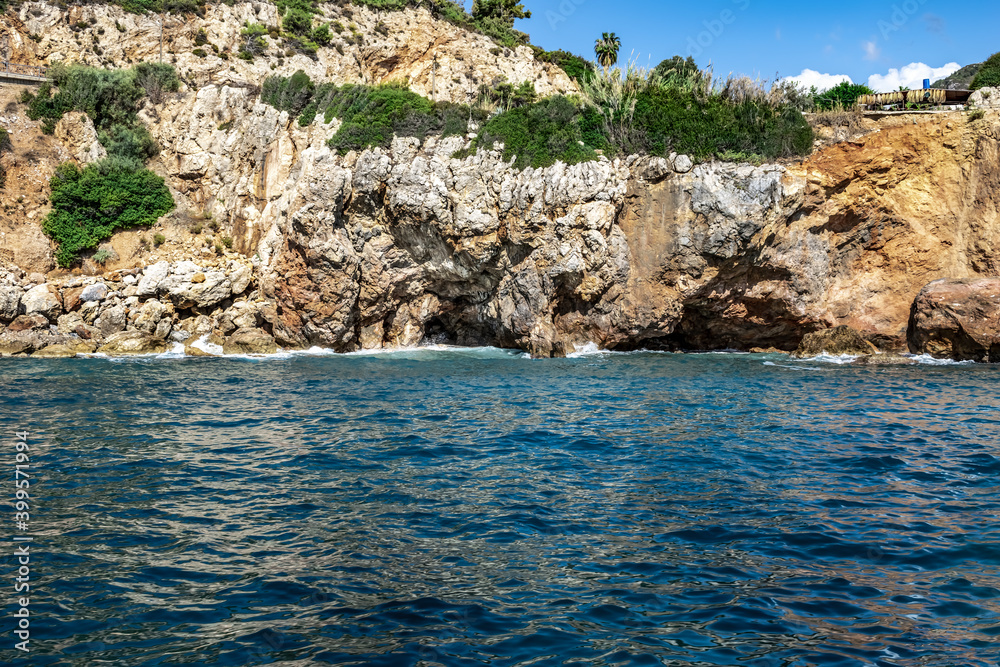 Rocky sandstone coast in Alanya (Turkey). Beautiful seascape with blue-turquoise water, brown-gray-yellow cliff and green plants growing on the bluff slopes