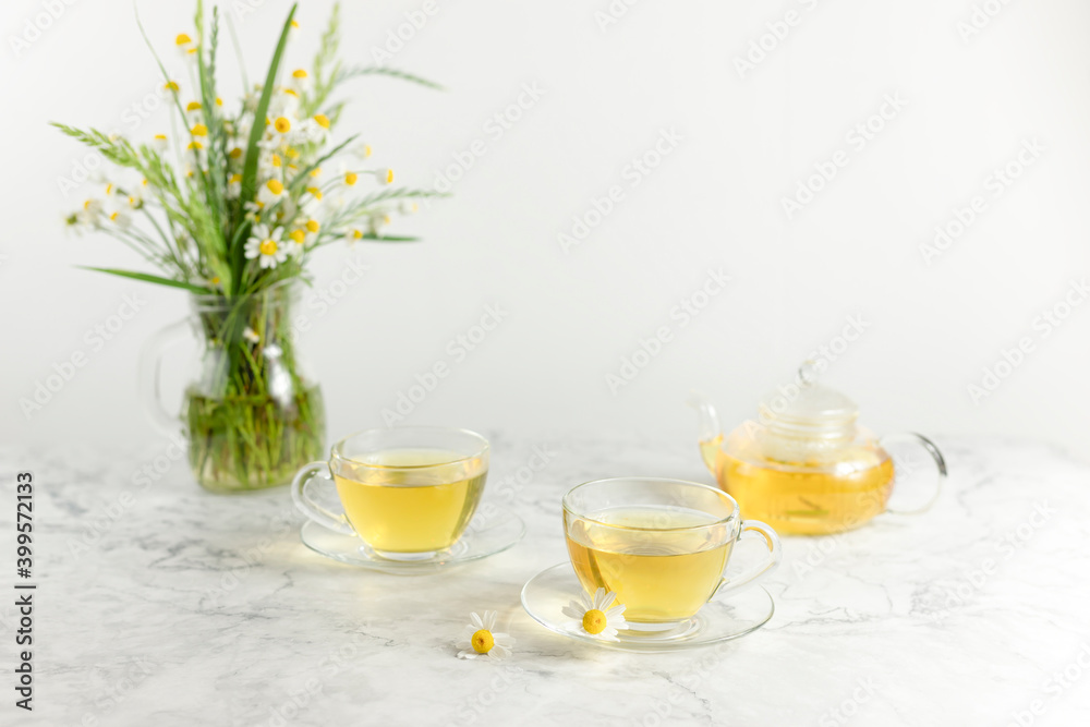 glass cups and teapot with chamomile tea on a white background. a bouquet of daisies.