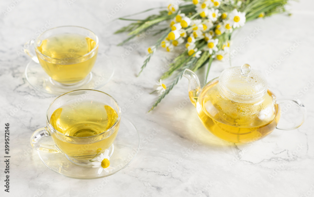 glass cups and teapot with chamomile tea on a white background. a bouquet of daisies. glass cups and teapot with chamomile tea on a white background. a bouquet of daisies.