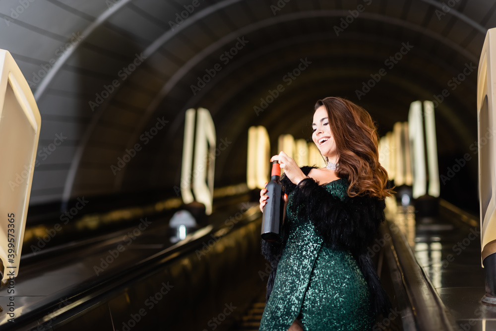 cropped view of glamour woman posing on escalator with bottle of wine