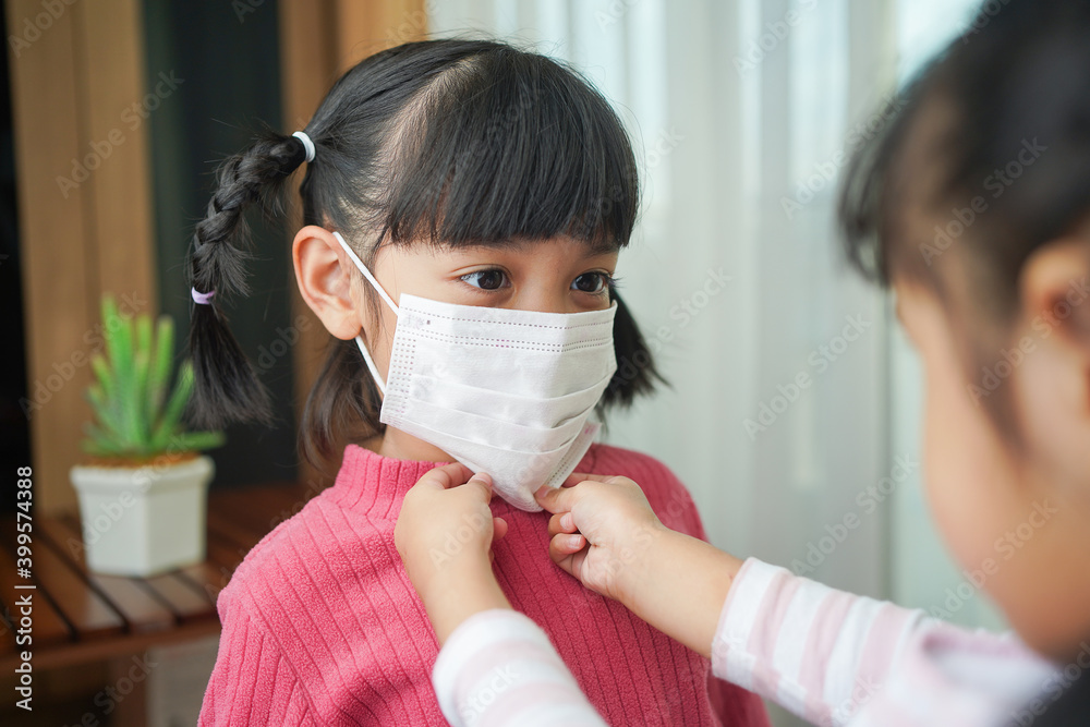 The sister helps the younger girl put on the surgical mask. Prevention of infection with coronavirus or Covid-19 infection