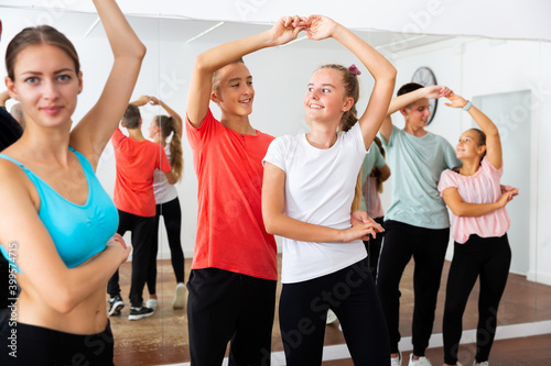 Teenagers dancing together slow ballroom dances in pairs in choreography class with young female trainer