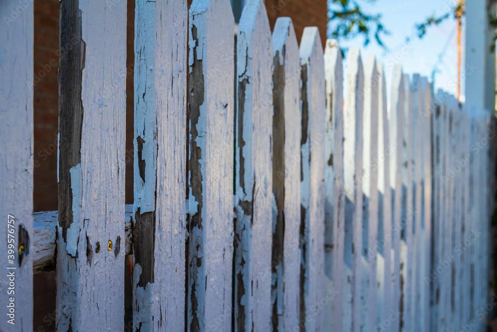 An old white picket fence with peeling paint in shadow.