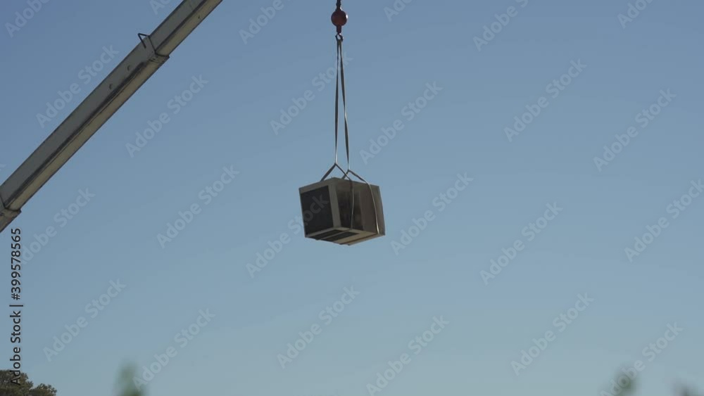 An old air conditioner unit being lifted off a roof by a crane