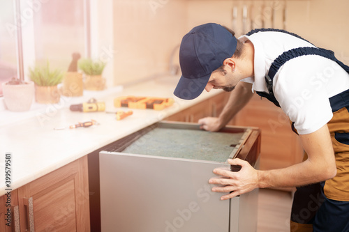 A man or service worker in special clothing installs, disassembles or performs maintenance of the built-in dishwasher