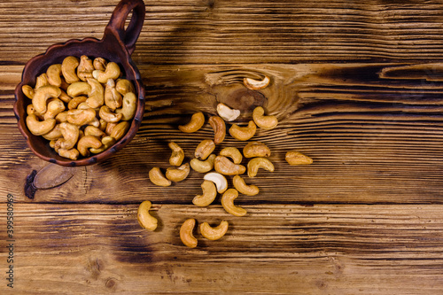 Ceramic bowl with roasted cashew nuts on a wooden table. Top view