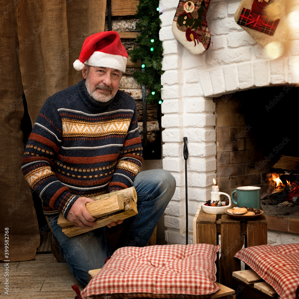 man in a Santa hat by the fireplace. Holds firewood in his hands. Christmas mood