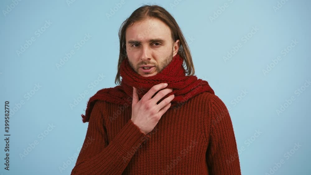 Man has a sore throat and coughing, looking unhappy and ill while posing against blue studio background Man has a sore throat and coughing, looking unhappy and ill while posing against blue studio background