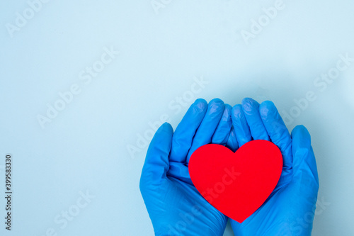Valentine's day during the coronavirus pandemic. Two hands in blue medical gloves holding a model in the shape of a red heart on a blue background, copy space, top view