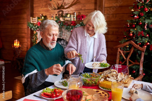 senior couple have meal sitting by served festive table on Christmas day  talk and smile  celebrate together at home