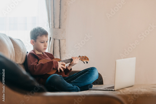 Boy playing ukulele and watching online course on laptop while practicing at home. Online training, online classes.Vintage color filter