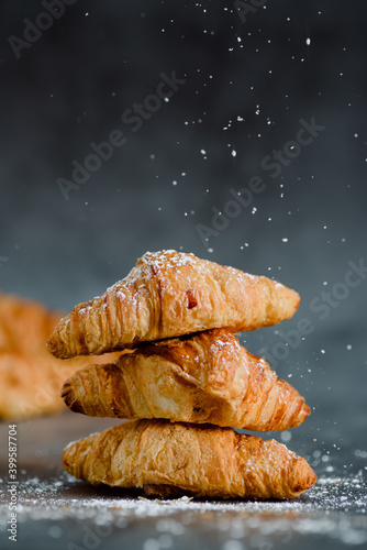 Close up of pile of delicious croissants on a dark background. Homemade croissants. Sugar glass falling. Vertical.
