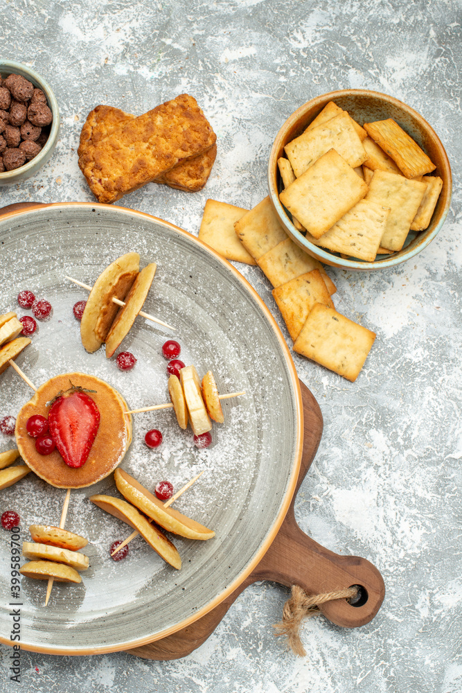 Fototapeta premium Vertical view of homemade pancakes and biscuits on wooden cutting board on blue backgound