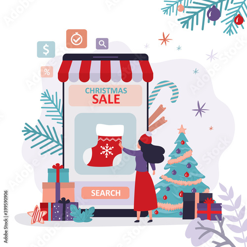 Cute woman chooses new year paraphernalia in online store. Christmas gift sock on smartphone screen