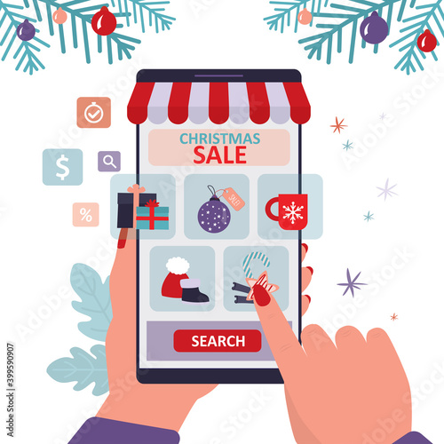 Hand holds smartphone with christmas accessories store on screen. Various new year paraphernalia presented in online shop