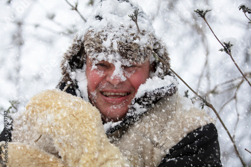 A frozen man covered in snow in winter smiles and looks at the camera. The first snow fell. A man in a fur hat in cold weather.